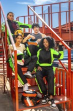 Group of diverse young people wearing racing suits and holding helmets, posing on metal stairs