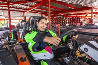 Woman in racing suit grips go kart steering wheel, seated on indoor track ready for competition,