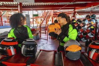 Diverse couple wearing racing suits, one partner kissing a helmet, getting ready for a go karting