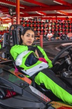Young woman in a bright green racing suit holding a helmet and sitting in a go kart, ready for a