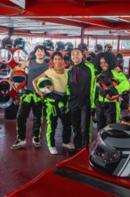 Group of diverse friends smiling and holding racing helmets, wearing go kart suits, and standing on