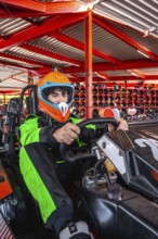 Young man wearing a racing suit and helmet, focusing on driving a go kart, preparing for a race at