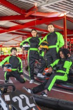 Diverse group of young people wearing racing suits and holding helmets, preparing for a fun karting