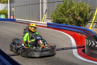 Person wearing a green racing suit and a yellow helmet is driving a go kart around a curve on an