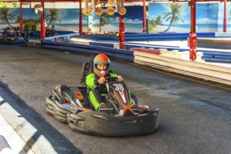 Man in orange helmet and green jumpsuit powering a go kart around a race track, pushing speed and