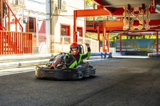 Go kart driver in helmet and racing suit crossing finish line on outdoor track, celebrating victory