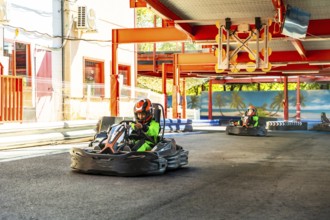 People wearing helmets and green racing suits driving go karts around an outdoor track, enjoying