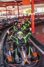 Group of excited people wearing helmets and racing suits, sitting in go karts and raising their