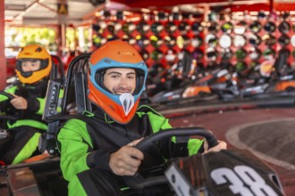 Young man wearing a colorful helmet and racing suit, smiling and driving a go kart on a track with
