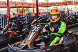 Young person wearing a bright green racing suit and orange helmet, sitting inside a go kart on the