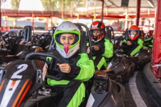 Young women in helmets and racing suits sit in go karts on an outdoor track, lined up and ready to