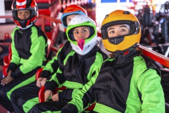 Young diverse friends in helmets and racing suits sit in go karts on an indoor track, ready and