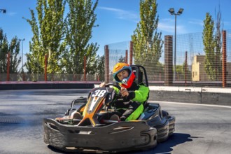 Young man in helmet and racing suit zooming a go kart on an outdoor asphalt track, enjoying speed