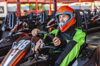 Man wearing an orange helmet and racing suit, sitting inside a go kart with the number 38, holding