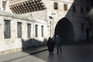 Istanbul, Turkey. January 3rd 2025. A Muslim couple walk behind Yeni Camii or New Mosque in the