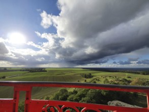View of green fields under dramatic sky with dark clouds, red railings in the foreground and
