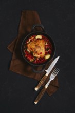 A chicken dish is served in a black cast iron pot. The pot contains spicy lingonberry sauce. Two