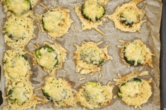 Broccoli pieces are smashed and spread on a baking sheet. They are topped with cheese and placed in