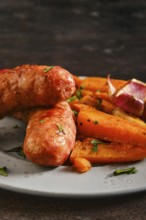 Natural casing sausages served with roasted carrots on a plate for a meal in a kitchen setting