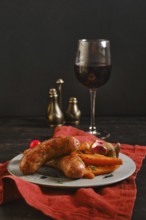 Sausages made with natural casings are placed on a plate with colorful vegetables. A glass of red