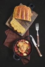 Top view of roasted chicken thigh with lingonberry in a pan on a brown cloth. Freshly baked bread