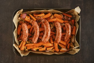 Natural casing sausages in a baking tray with sweet potatoes and onions. The tray contains roasted