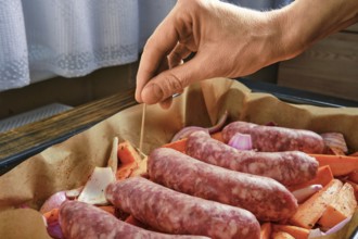 A hand is pierces a toothpick into natural casing sausages arranged on a tray with chopped