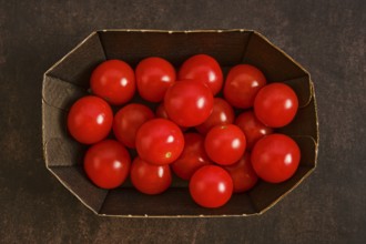 Cardboard box holds many red cherry tomatoes. The tomatoes are bright and round, placed together