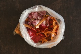 A clear plastic bag holds various vegetable peels and scraps. The bag sits on a dark countertop,