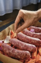 A hand is placing a toothpick into natural casing sausages that rest on a bed of sweet potatoes and