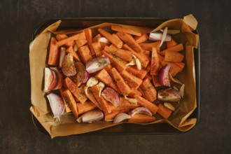 Top view of sweet potatoes, red onion and garlic seasoned on parchment lined tray, prepared for