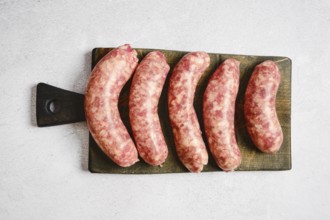 Five natural casing sausages on a wooden cutting board. They appear fresh and raw with visible meat