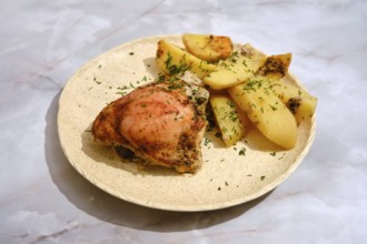 A portion of baked chicken is placed on a plate alongside cut potatoes. The chicken has a bit of
