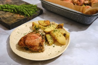 Food is arranged on a plate with roasted chicken and potatoes. Fresh herbs are visible on the food.