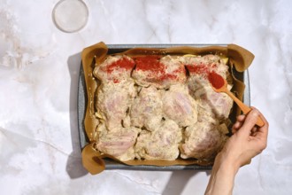 A person spreads smoked paprika over chicken thighs placed in a baking tray lined with parchment