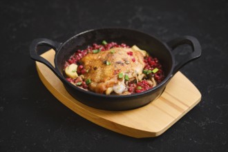 A cast iron skillet holds a serving of cooked chicken topped with lingonberry and chopped spring