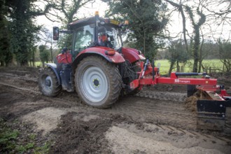 Tractor grading and levelling work repair a muddy, flood-prone country lane, Sutton, Suffolk