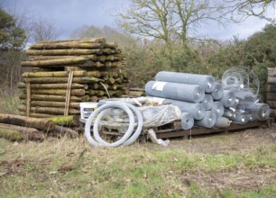Agricultural fencing supplies wooden fence posts, rolls of wire stacked outdoors post-and-wire