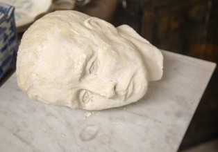 Human head and face plaster death mask or sculpture artwork on its side on marble, UK