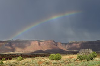 Bright rainbow stretches across a dramatic desert landscape with rocks and threatening sky,