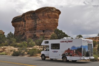 Motorhome standing on a road in front of a distinctive rock formation under a cloudy sky,