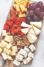 Assorted cheese on a wooden board, with grapes and walnuts, appetizer, no people