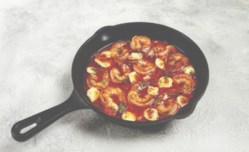 Greek saganaki, in an iron pan, saganaki with shrimp, shrimp in tomato sauce, with pepper and feta