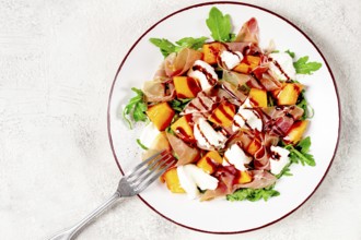 Salad with slices of ripe melon, prosciutto, mozzarella and fresh arugula, decorated with balsamic