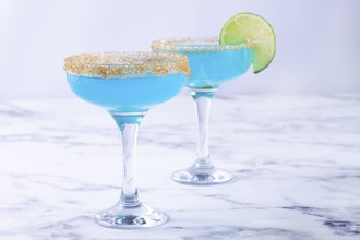 Colorful blue cocktails in elegant glasses with lime garnish on a marble table
