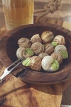 Snails cooked with herb oil on a wooden plate, served with white wine, natural light, no people