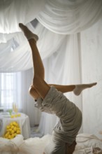 A person is upside down in a yoga pose in a bright room. The space is filled with white drapes and
