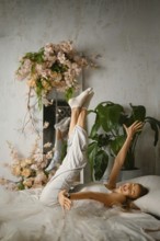 A woman is lying on a bed with white sheets. She lifts her legs and moves her arms freely.