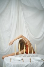 A woman is seen bending gracefully at a table set with candles. The table has white plates and