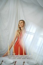 A woman stands near a table that has candles, plates, and cutlery. The soft light comes through the